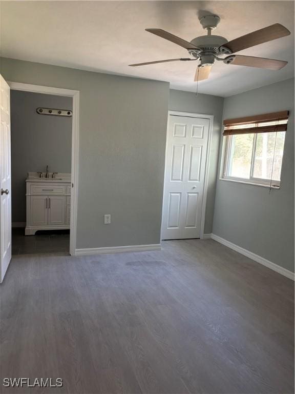 unfurnished bedroom with wood finished floors, ensuite bathroom, baseboards, and a sink