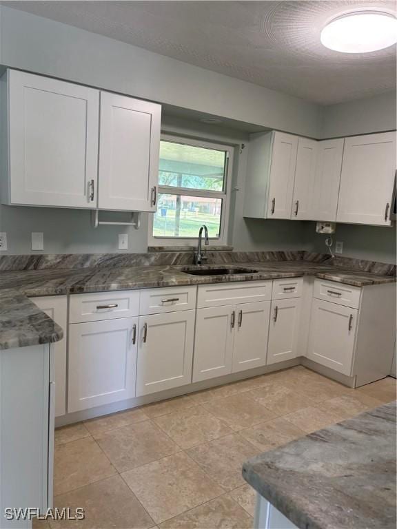 kitchen featuring dark stone counters, white cabinetry, and a sink