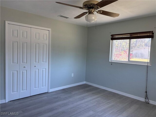 unfurnished bedroom featuring wood finished floors, a closet, visible vents, baseboards, and ceiling fan