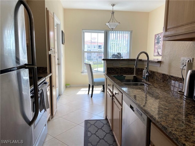 kitchen with hanging light fixtures, a sink, a peninsula, dark stone countertops, and appliances with stainless steel finishes