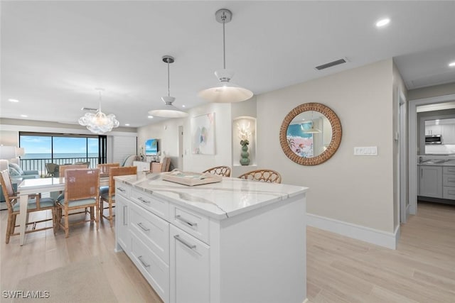 kitchen with recessed lighting, hanging light fixtures, light stone counters, visible vents, and light wood-style floors