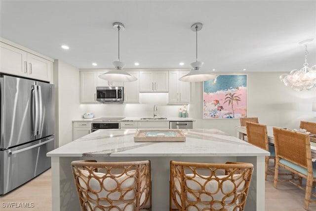 kitchen with a center island, a sink, stainless steel appliances, white cabinets, and light stone counters