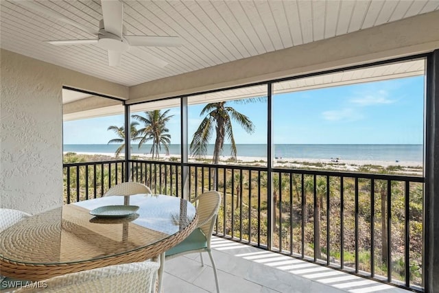sunroom with a water view, a view of the beach, and a textured wall