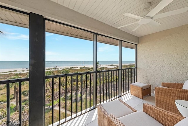sunroom with a water view, a ceiling fan, and a view of the beach