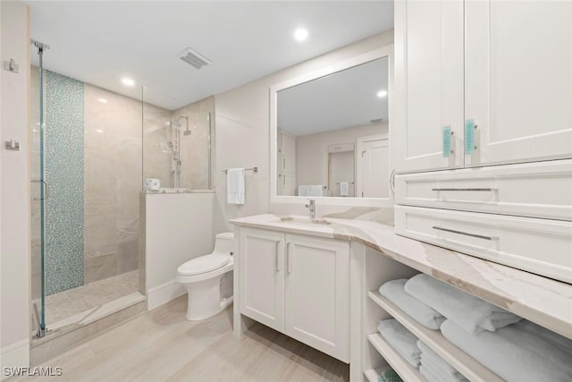 bathroom featuring toilet, vanity, wood finished floors, and a walk in shower