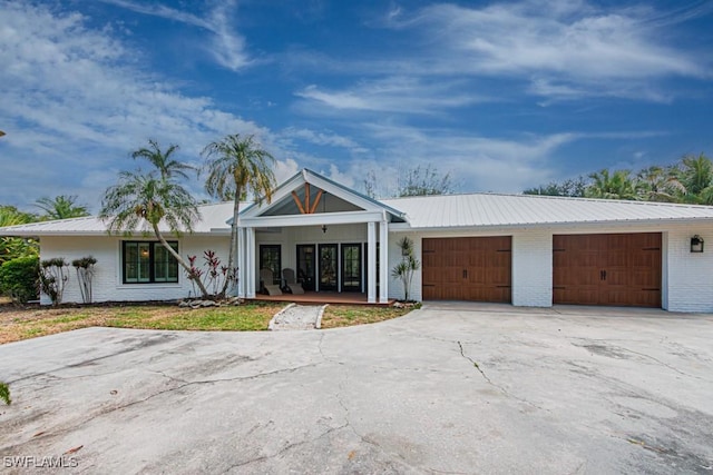 view of front of home featuring brick siding, driveway, an attached garage, and metal roof