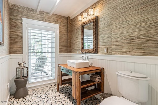 half bathroom featuring wainscoting, beamed ceiling, toilet, healthy amount of natural light, and vanity
