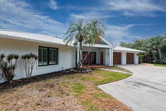 view of front of property with brick siding, concrete driveway, an attached garage, covered porch, and metal roof
