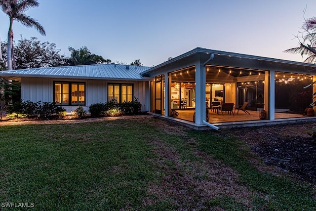 back of property at dusk featuring a sunroom, a yard, metal roof, and board and batten siding