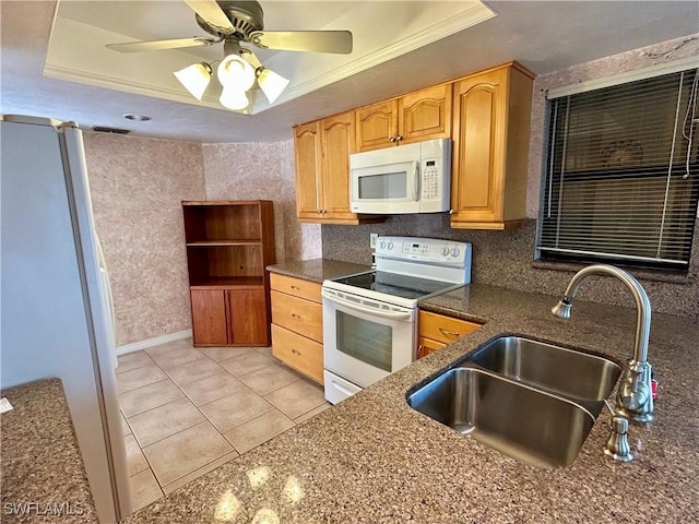 kitchen featuring white appliances, a raised ceiling, a sink, crown molding, and dark stone countertops