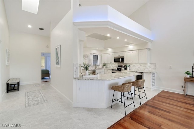 26271 Devonshire Ct Unit 202, Bonita Springs, FL 34134 - kitchen with appliances with stainless steel finishes, a towering ceiling, light stone counters, white cabinets, and a peninsula