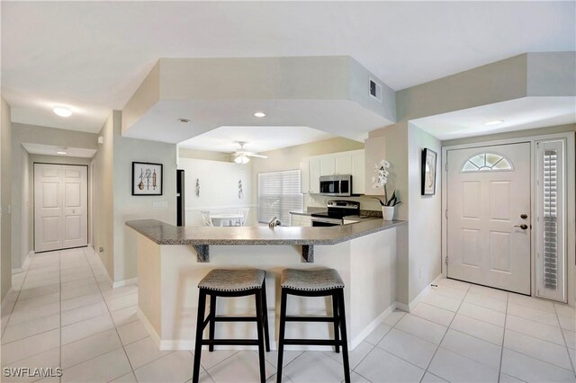 10910 Santa Margherita Rd Unit 101, Estero, FL 34135 - kitchen featuring appliances with stainless steel finishes, light tile patterned flooring, white cabinets, a kitchen bar, and a peninsula