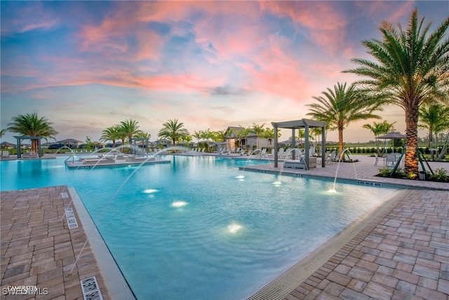 pool at dusk featuring a patio and a community pool
