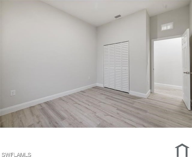unfurnished bedroom featuring baseboards, visible vents, a high ceiling, and wood finished floors