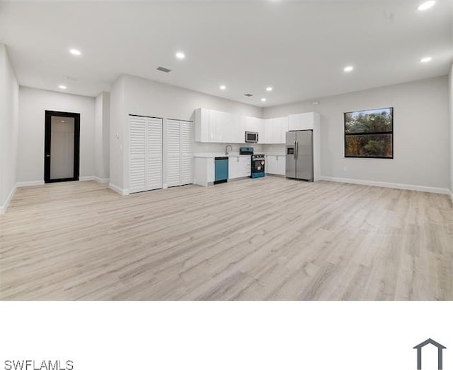 interior space featuring recessed lighting, open floor plan, stainless steel appliances, white cabinets, and light wood-type flooring