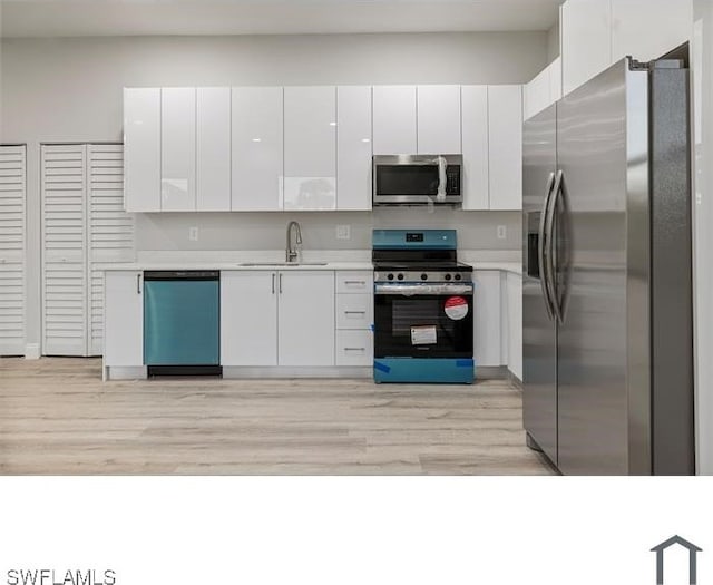 kitchen with light wood-style flooring, a sink, white cabinets, light countertops, and appliances with stainless steel finishes