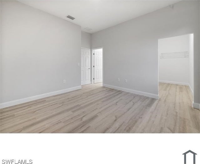unfurnished room featuring baseboards, light wood-style floors, and lofted ceiling
