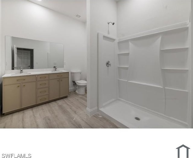 bathroom with toilet, a sink, double vanity, wood finished floors, and a shower