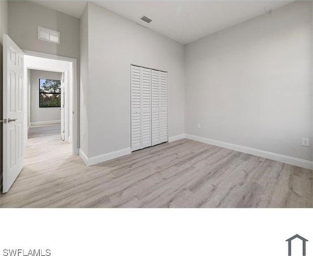 unfurnished bedroom with baseboards, a closet, light wood finished floors, and visible vents