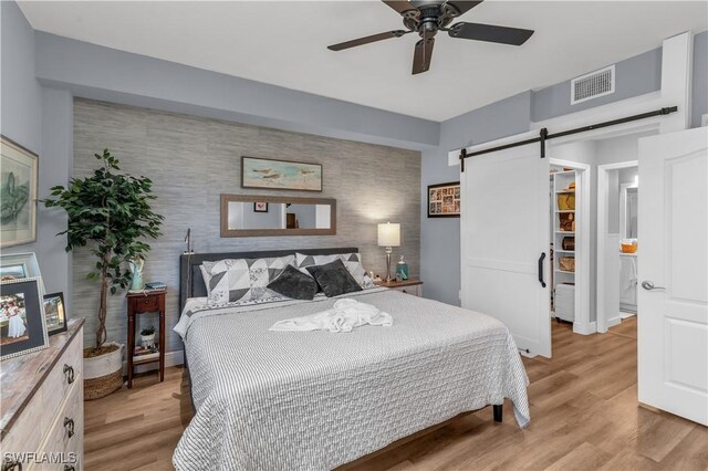 350 Newport Dr Unit 1902, Naples, FL 34114 - bedroom featuring an accent wall, a barn door, light wood-type flooring, a ceiling fan, and baseboards