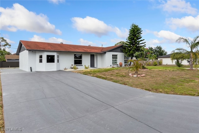 ranch-style house featuring stucco siding, a front lawn, and driveway