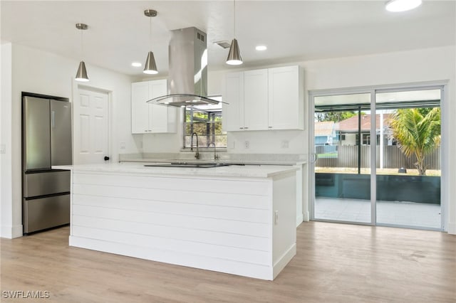 kitchen featuring freestanding refrigerator, island exhaust hood, light countertops, and a healthy amount of sunlight