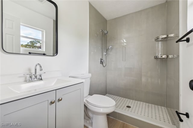 full bathroom with vanity, toilet, wood finished floors, and a tile shower