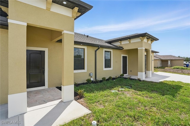 doorway to property with a lawn, stucco siding, and roof with shingles