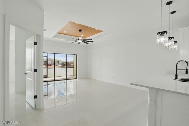 unfurnished living room featuring a tray ceiling, a sink, ceiling fan, baseboards, and recessed lighting