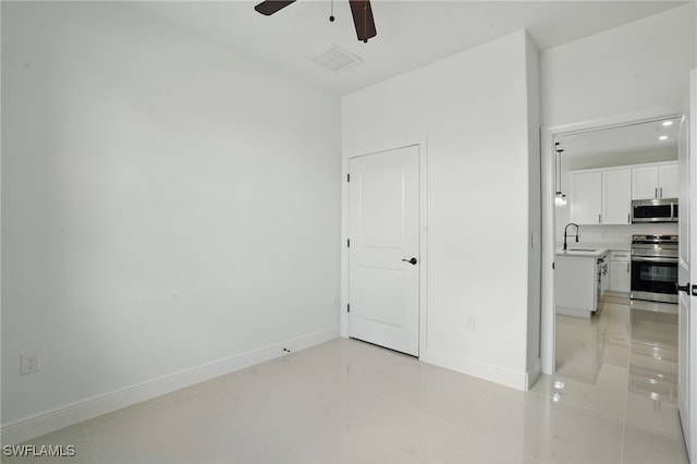 unfurnished room with a sink, a ceiling fan, baseboards, and light tile patterned floors