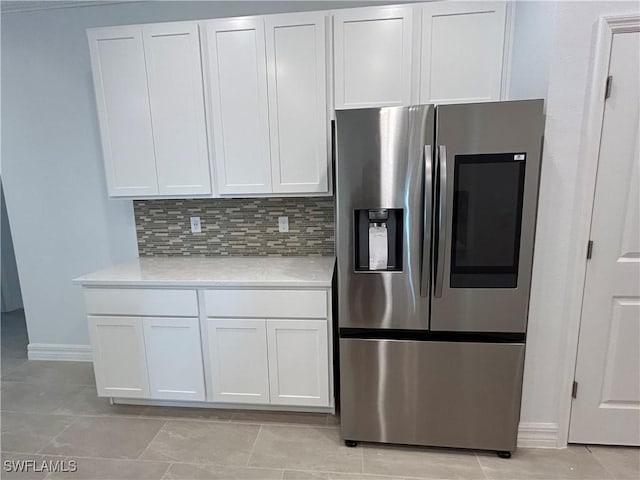 kitchen with baseboards, stainless steel fridge, backsplash, light countertops, and white cabinets