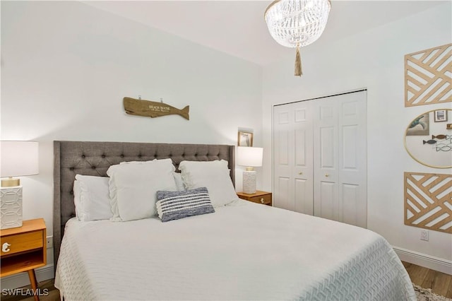 bedroom featuring wood finished floors, a chandelier, baseboards, and a closet
