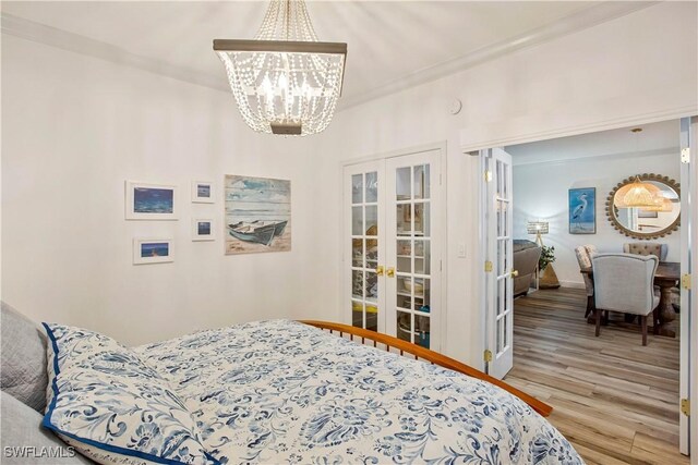 bedroom featuring french doors, a chandelier, wood finished floors, and baseboards