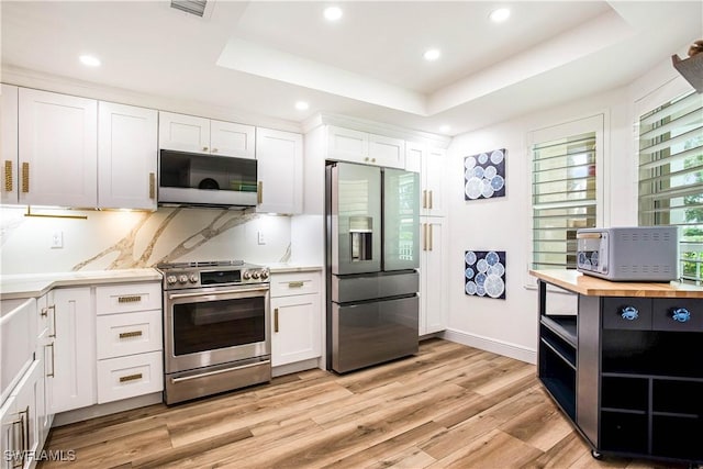 kitchen featuring appliances with stainless steel finishes, wooden counters, a raised ceiling, light wood finished floors, and white cabinetry