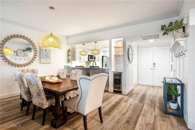 dining space featuring beverage cooler, light wood-style floors, crown molding, and baseboards
