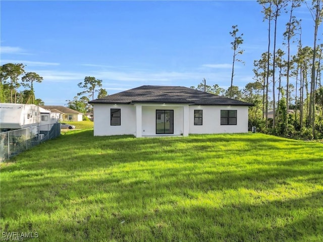 rear view of property featuring a yard, roof with shingles, fence, and stucco siding