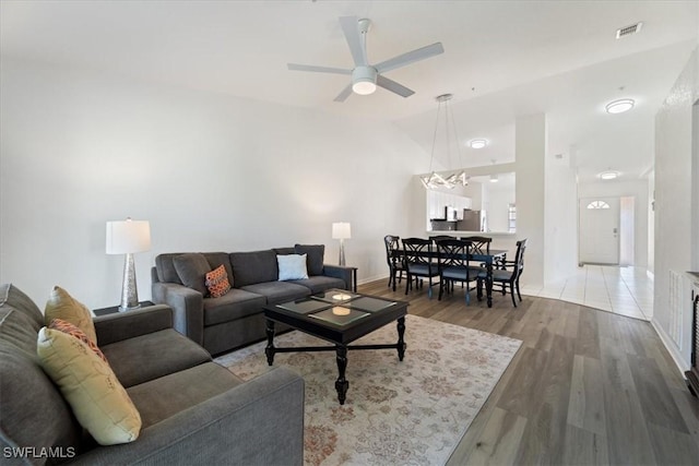 living area featuring ceiling fan, wood finished floors, vaulted ceiling, a chandelier, and baseboards