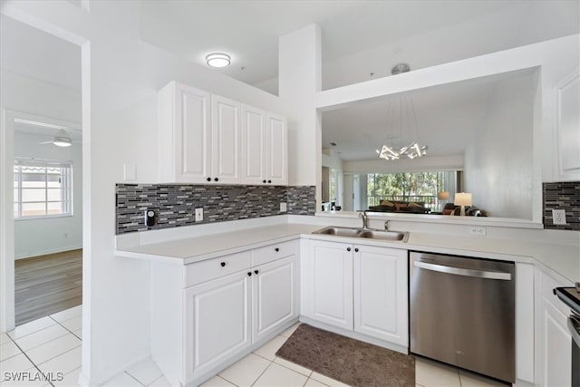 kitchen featuring stainless steel dishwasher, a sink, backsplash, light countertops, and a chandelier