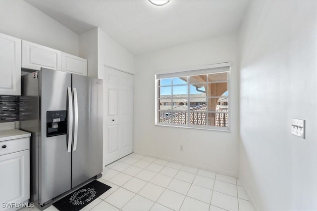 kitchen with stainless steel refrigerator with ice dispenser, white cabinetry, light countertops, and baseboards