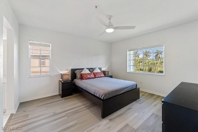 bedroom featuring light wood-style floors, multiple windows, baseboards, and a ceiling fan