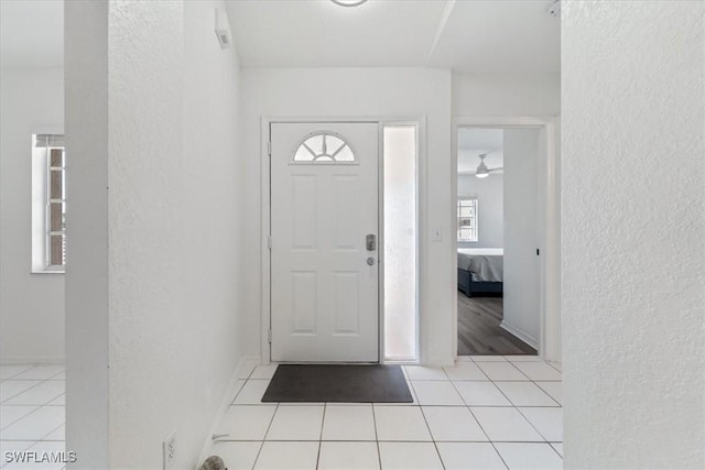 foyer with a textured wall, light tile patterned flooring, and a ceiling fan