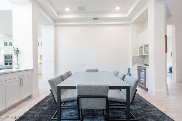 dining space featuring a dry bar, wine cooler, light wood-type flooring, visible vents, and a tray ceiling