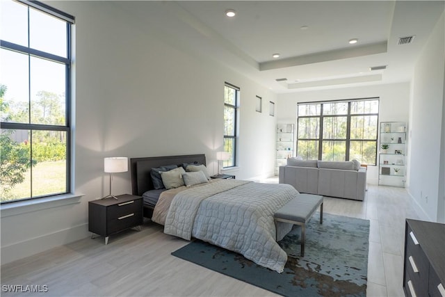 bedroom featuring a tray ceiling, light wood finished floors, baseboards, and visible vents