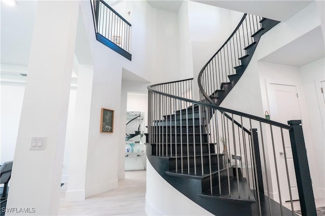 staircase with wood finished floors, baseboards, and a high ceiling