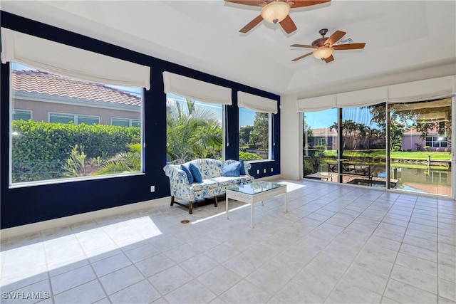 sunroom / solarium with a water view, tile patterned flooring, a ceiling fan, and a raised ceiling