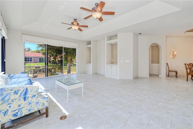 unfurnished living room with a tray ceiling, ceiling fan, and arched walkways