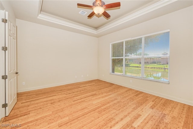 empty room with a tray ceiling, ornamental molding, ceiling fan, visible vents, and light wood-style floors