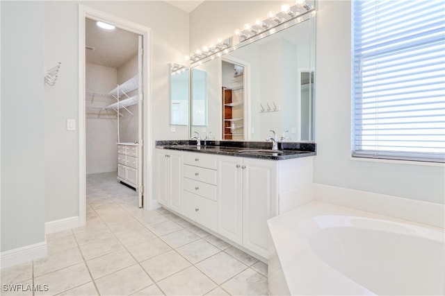 full bath featuring a sink, tile patterned floors, a garden tub, double vanity, and a walk in closet