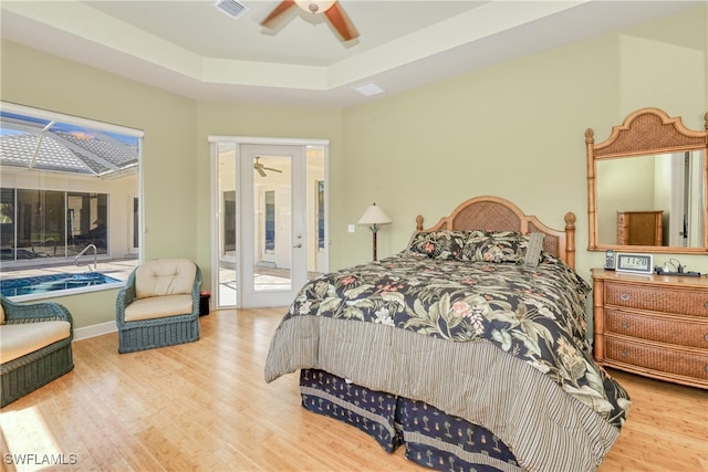 bedroom featuring wood finished floors, access to exterior, visible vents, a raised ceiling, and ceiling fan