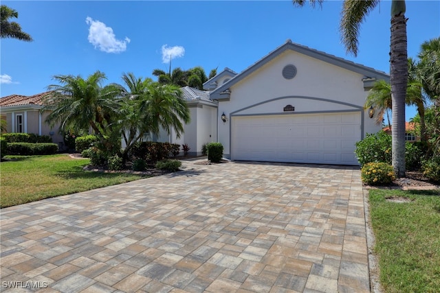 view of front of property with a tiled roof, decorative driveway, an attached garage, stucco siding, and a front lawn